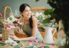 a smiling lady is sitted on the table where beautiful flowers are keeping in the basket to hangout in the home decor enhancement